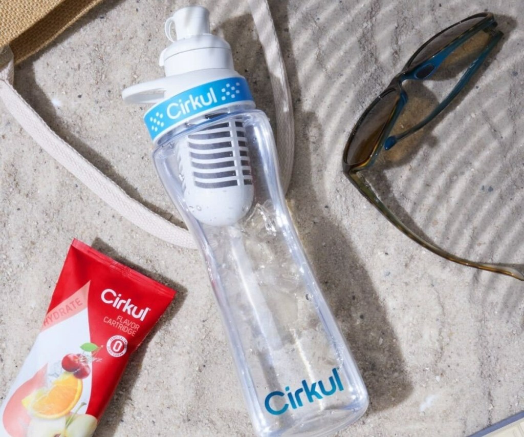 water bottle on sand next to sunglasses and beach bag