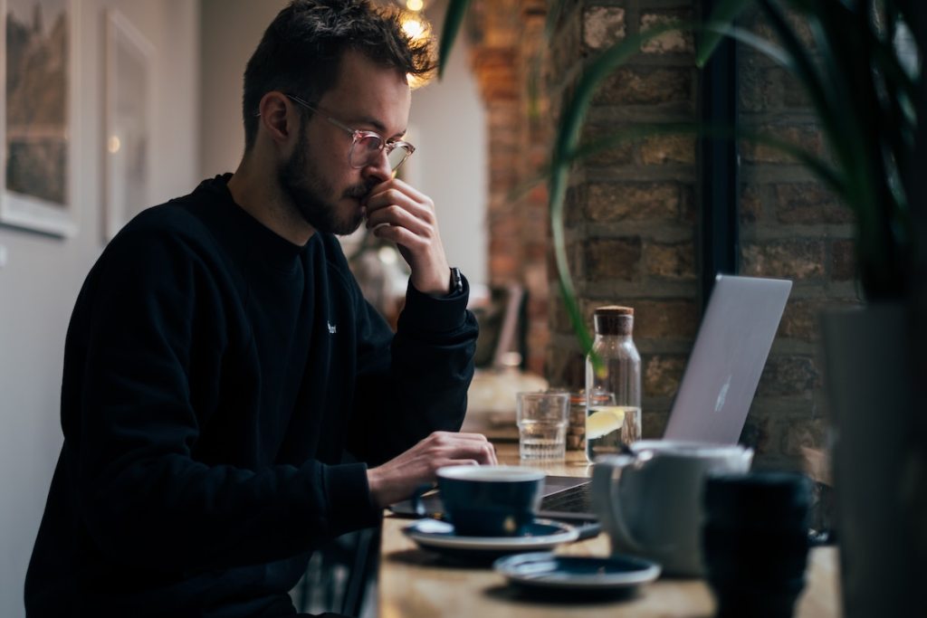 man with glasses sitting at desk on laptop