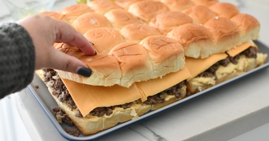 Putting the tops of Hawaiian rolls back on sliders before baking. 