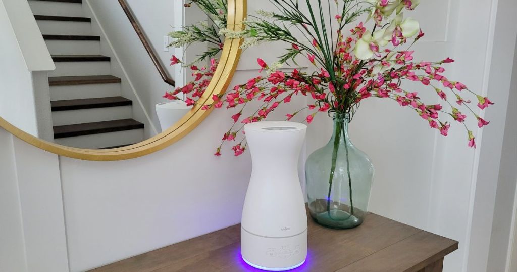 white Anjou diffuser with purple light placed on wood table beside plant