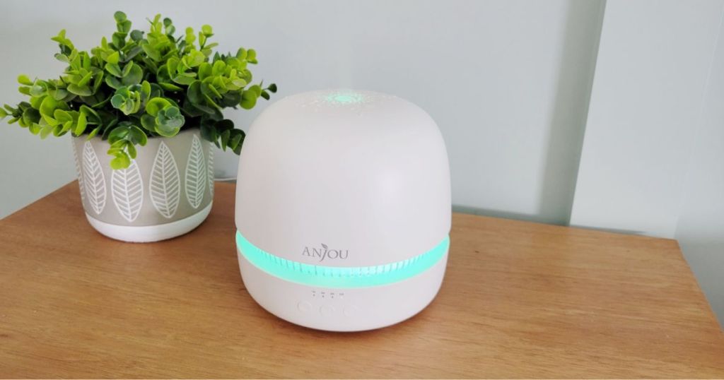 white Anjou diffuser with blue light places on wood table beside plant