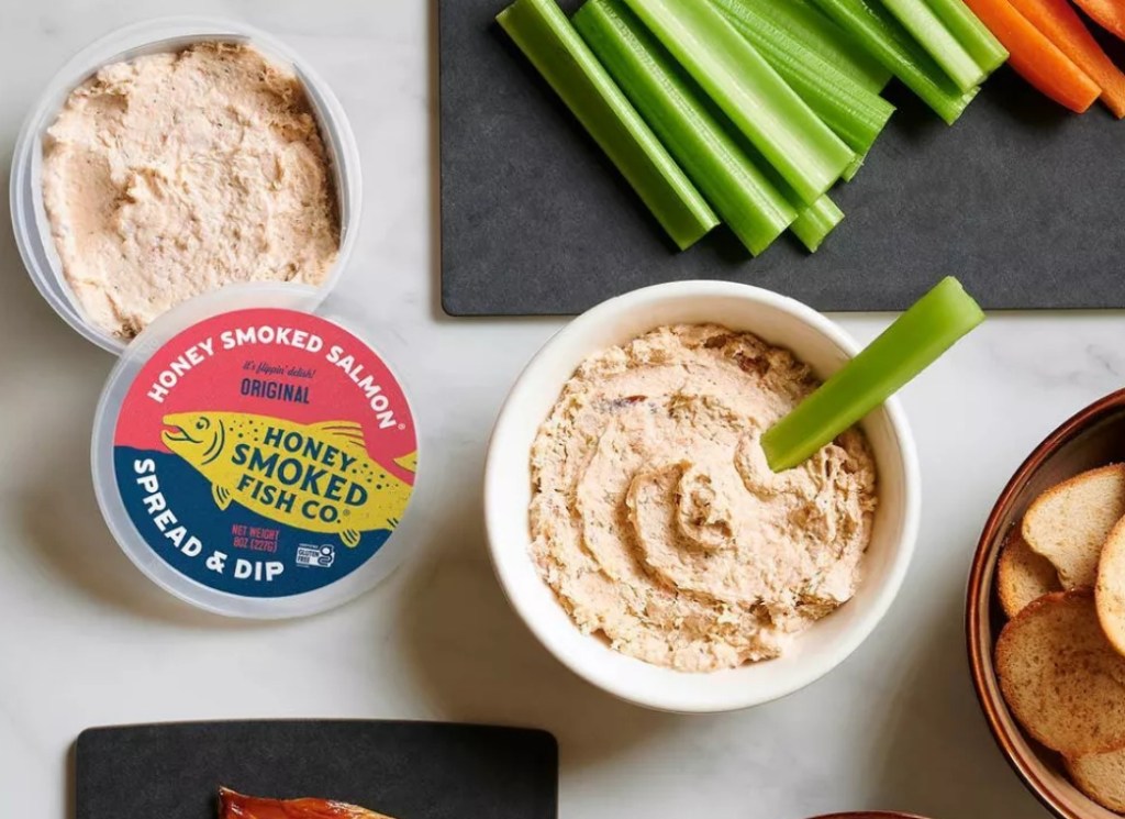 Honey Smoked Fish Co. Salmon Original Greek Yogurt Dip open with the lid to the side and some in a bowl with a stick of celery in the bowl