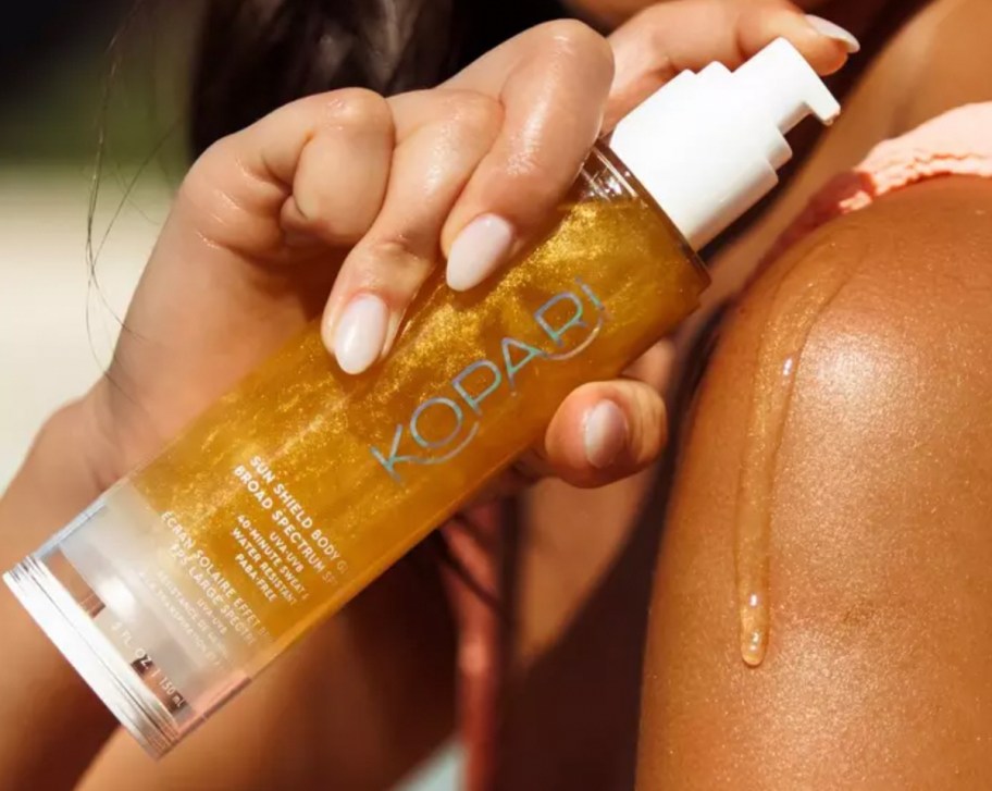 hand holding Kopari Beauty Sun Shield SPF 50 over tan skin dripping down shoulder
