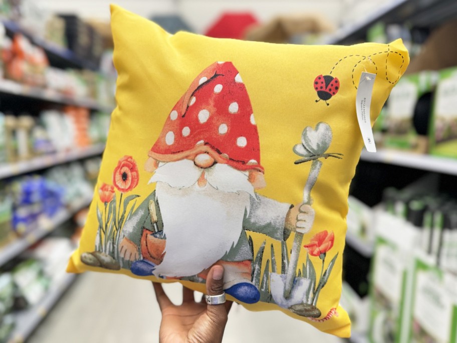 hand holding a yellow throw pillow with a garden gnome on it