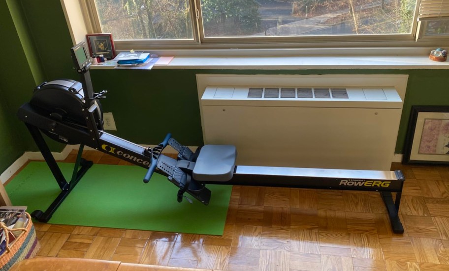 rowing machine on green mat and hardwood floor next to window