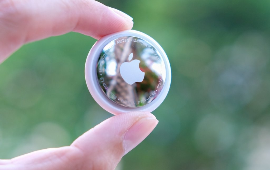 close up of fingers holding apple airtag in front of greenery