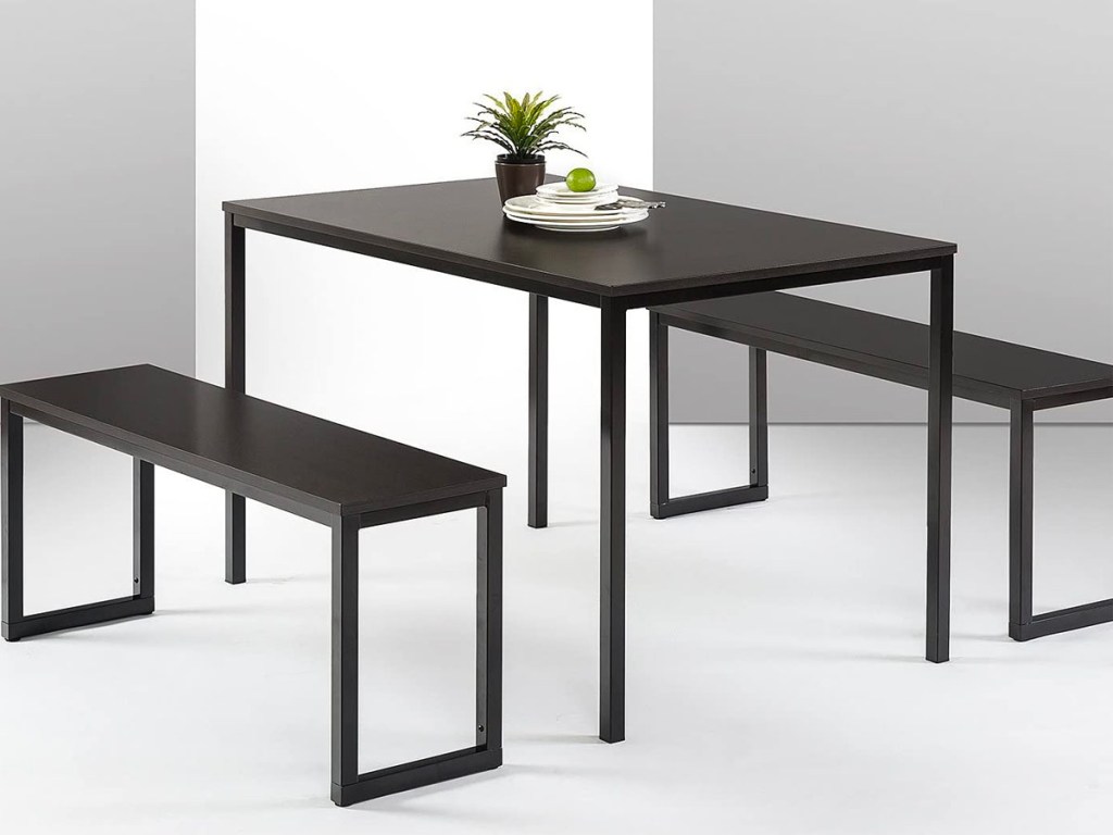 black dining table with two bench seats with plate and plant on top 