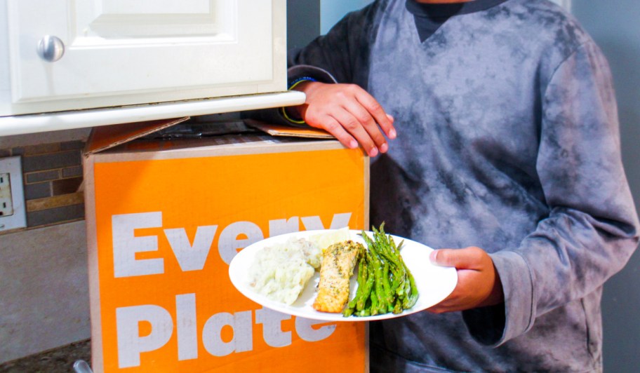 person holding plate of food near everyplate box