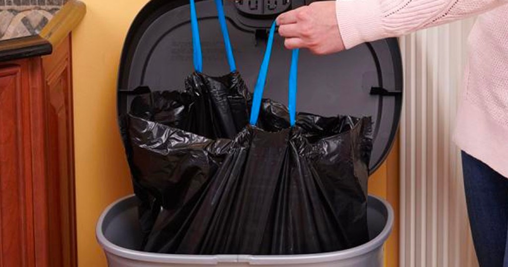 woman lifting hefty black trash bag out of trash can