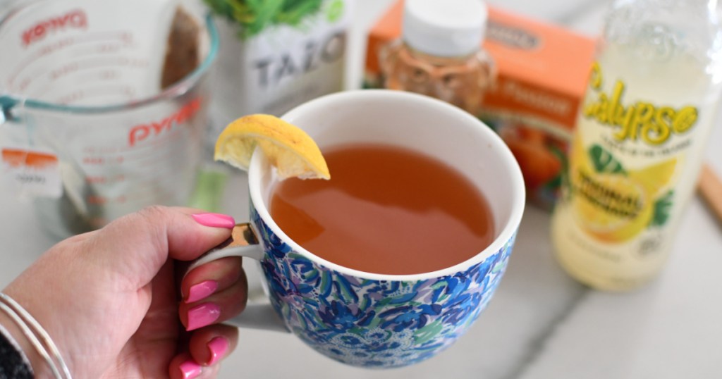 holding a cup of homemade medicine ball tea next to ingredients