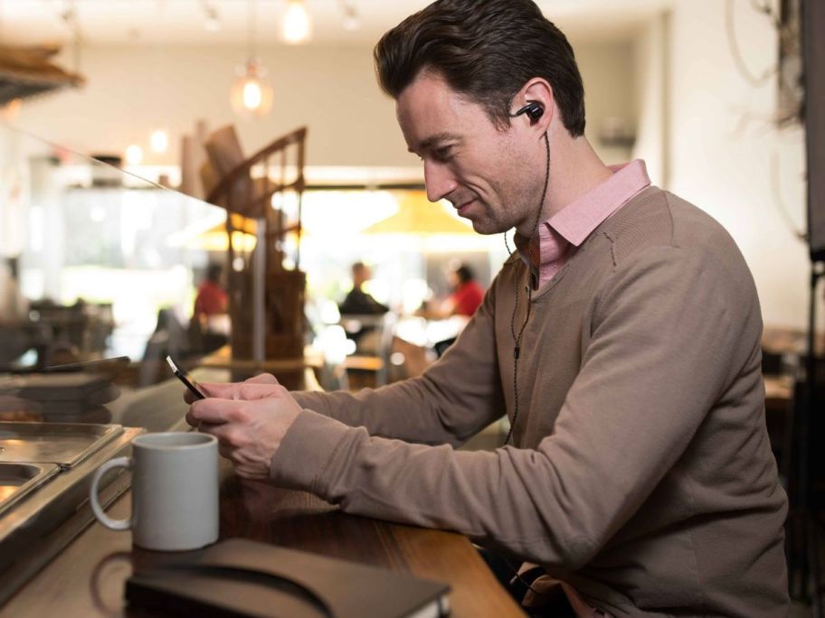 Man drinking coffee in a coffee shop while wearing AKG headphones