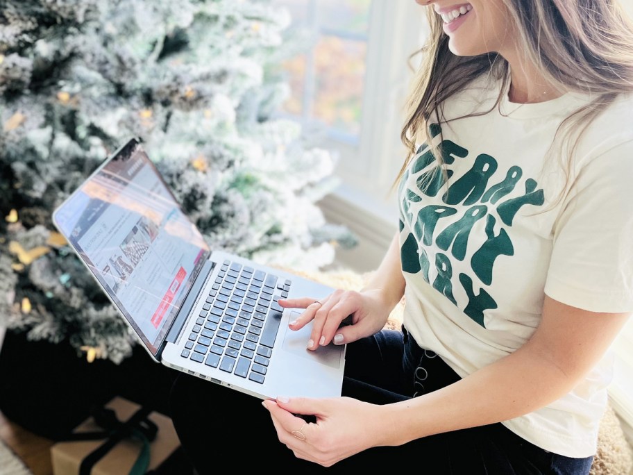 woman on a macbook displaying hip2save near christmas tree