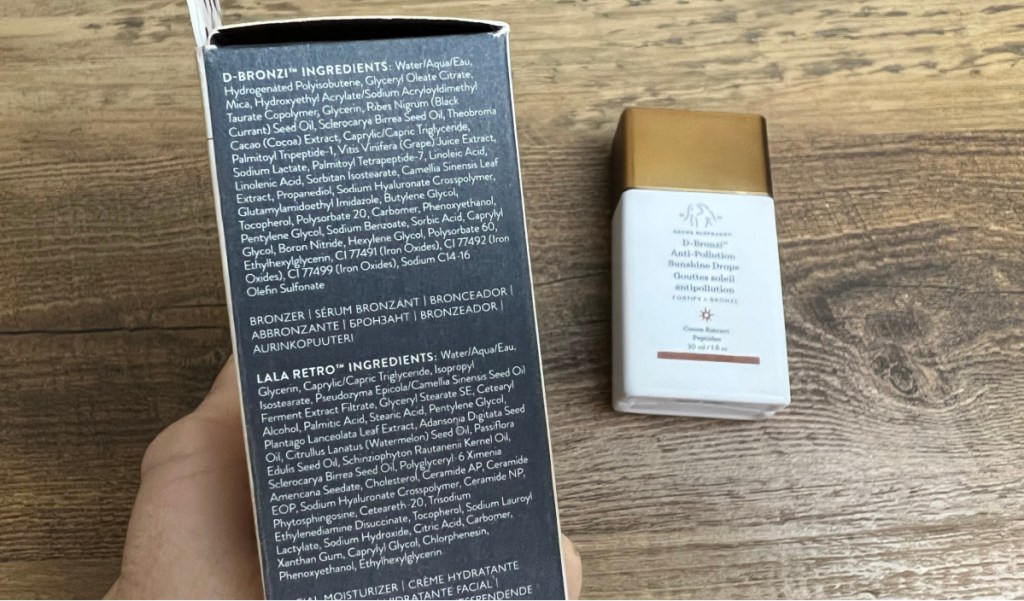 woman showing the ingredient list on the back of the drunk elephant bronzer drops package