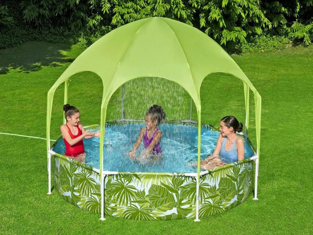 Three kids playing in a pool with a green shade above them