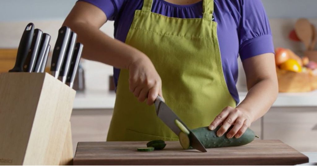 Woman chopping a cucumber with the Amazon Basics 9-Piece Premium Kitchen High-Carbon Stainless-Steel Blades with Pine Wood Knife Block Set, Black