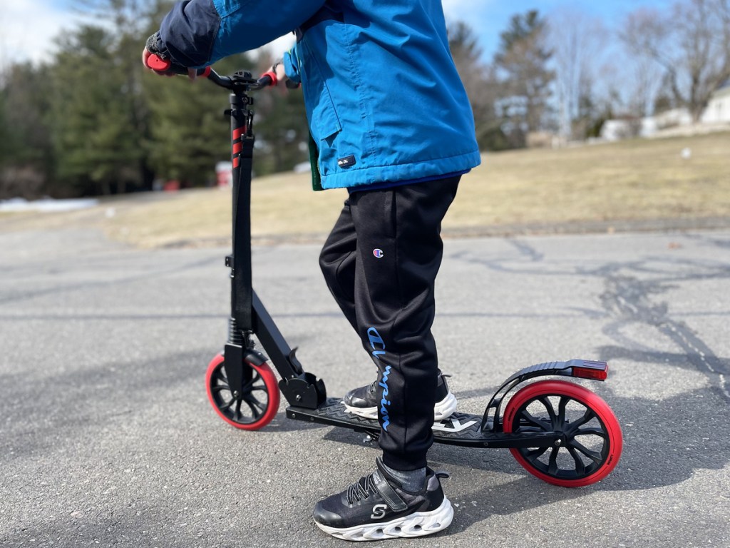 boy standing on a black and red scooter