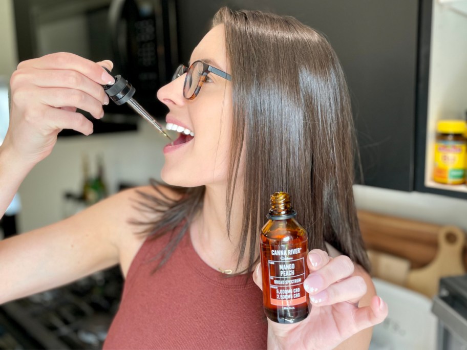 woman taking cbd tincture under tongue with dropper