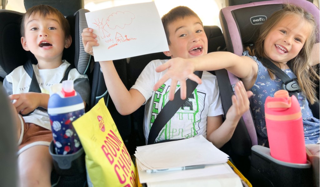 three kids in backseat of car with water bottles and toys