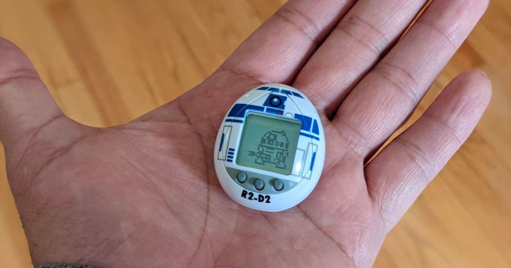 a mans hand holding a r2 d2 tamagotchi