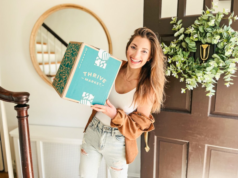 woman holding thrive market box in foyer by front door