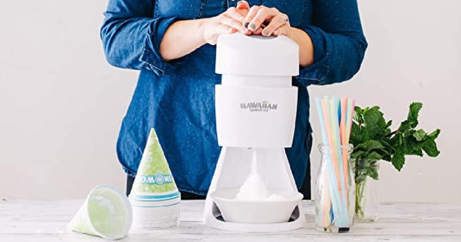 woman pressing down on the Hawaiian Shaved Ice S900A Shaved Ice and Snow Cone Machine with snow cones around