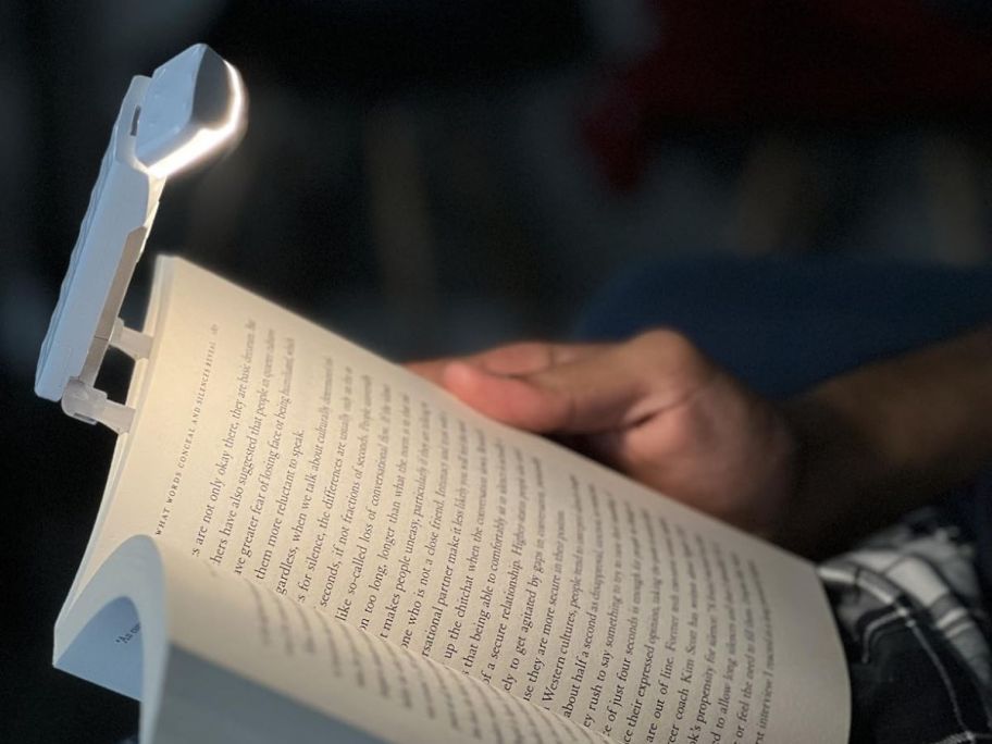 hand holding a book with a clip on book light attached shining light onto the book