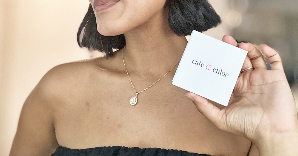 woman wearing a gold teardrop necklace and holding up jewelry box