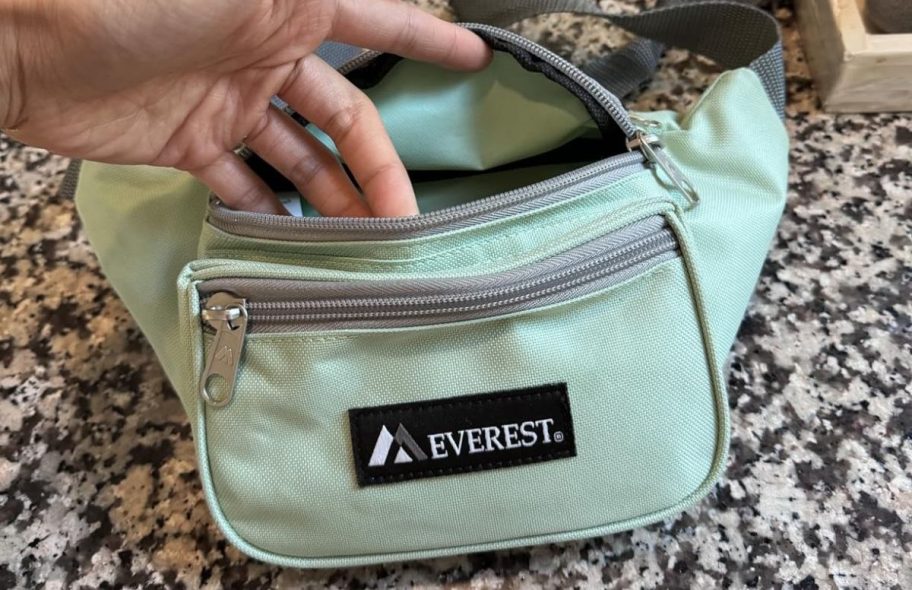 a womans hand opening a jade green belt bag