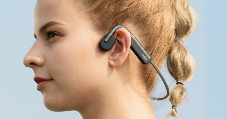 woman wearing a pair of black and silver over ear headphones that go around the back of her neck instead of over her head