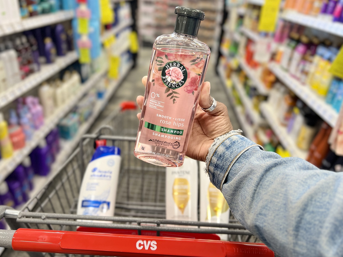 hand holding a bottle of herbal essences shampoo in front of cvs shopping cart