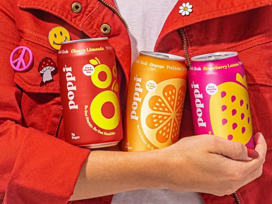 woman holding 3 different cans of poppi soda