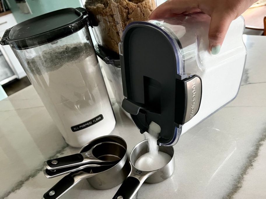 hand using a Prokeeper+ storage container to pour sugar into a measuring cup 