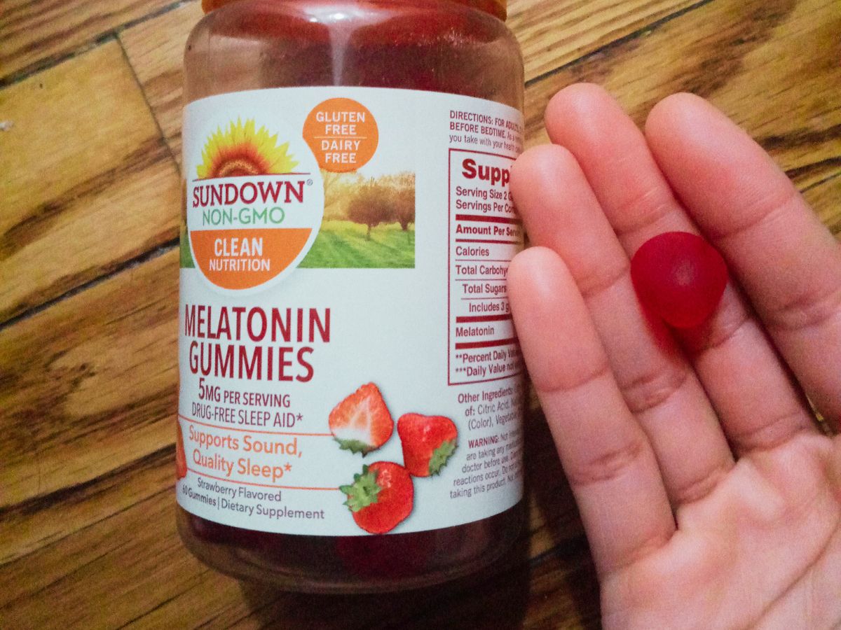 bottle of Sundown Melatonin Gummies with hand holding gummy next to bottle