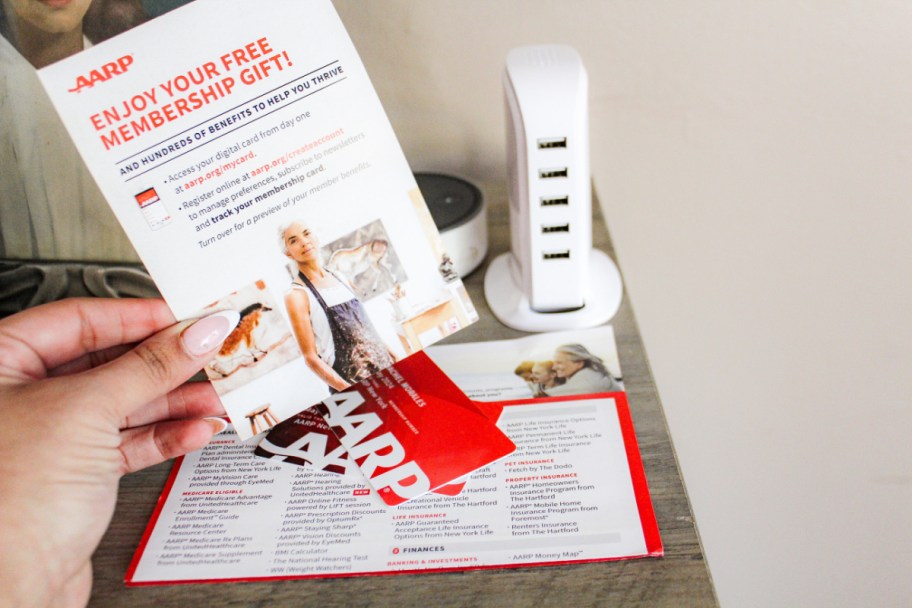 hand holding a welonlinee letter above aarp membership cards and a charging hub