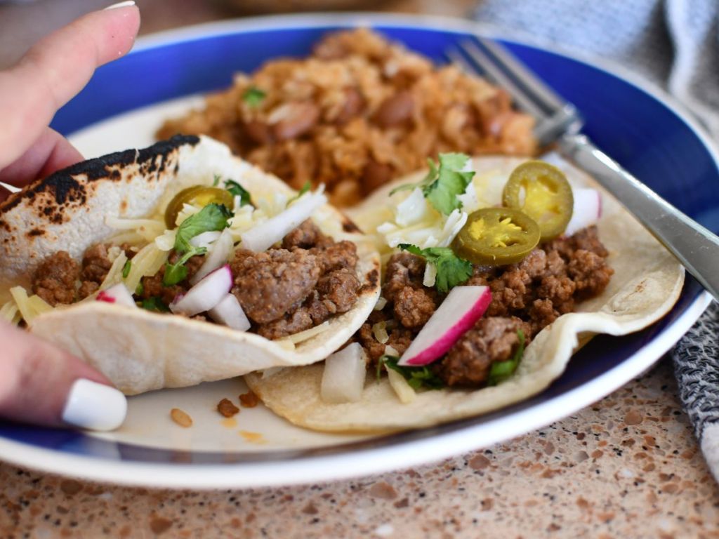 person taking taco from plate of tacos