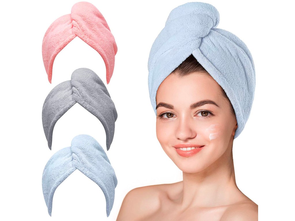 woman wearing blue hair towel with pink, gray and blue hair towels next to her. 