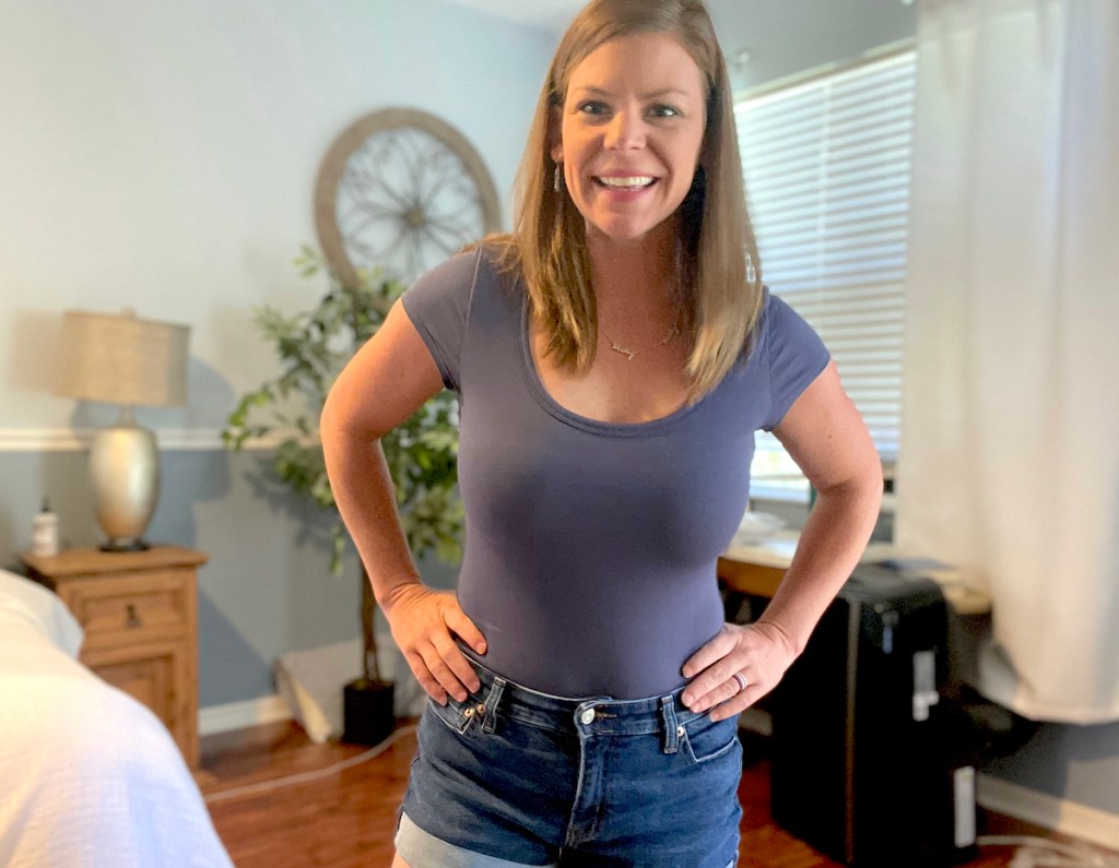 woman smiling with hands on hips wearing jean shorts and short sleeve bodysuit