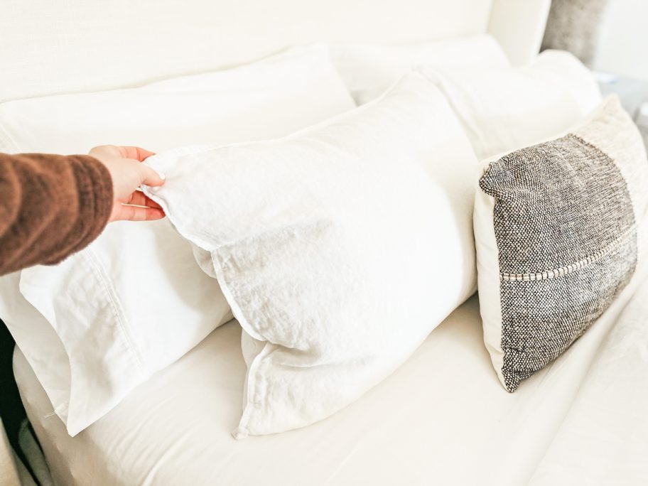 hand holding corner of white linen pillow for how to make a bed like boll and branch