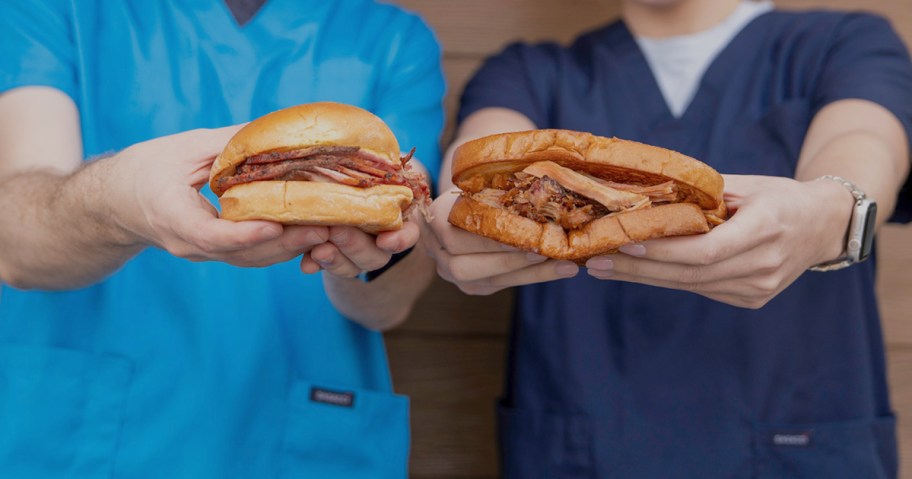 two people wearing scrubs and holding BBQ sandwiches 