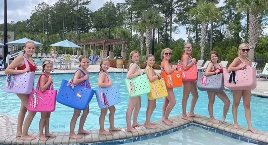 several women and girls standing in a line near pool with colorful bag