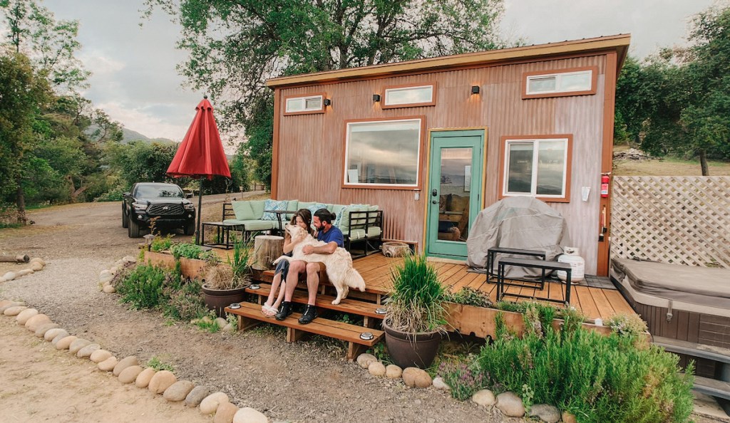 couple with dog on lap sitting in front of cute tiny home