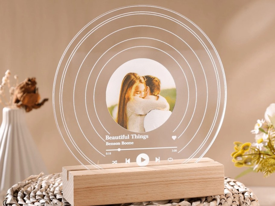 a clear vinyl record on a wood stand with a photo of a man and woman hugging and the name of a song