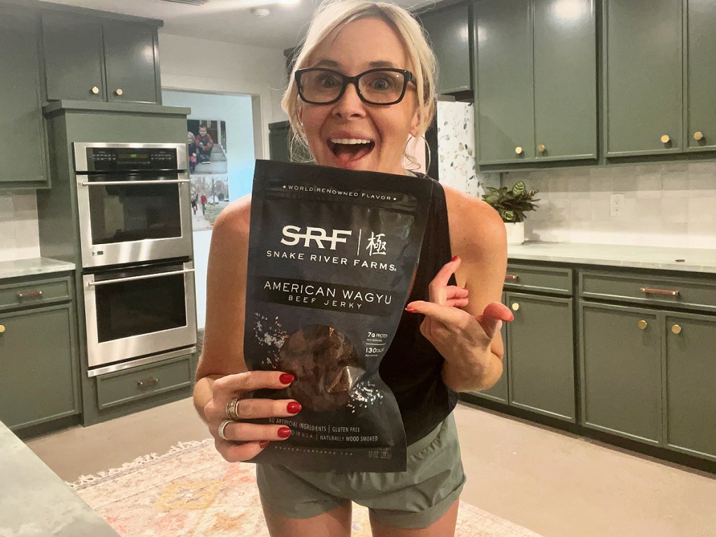 woman holding bag of Snake River Farms Jerky in her kitchen and smiling