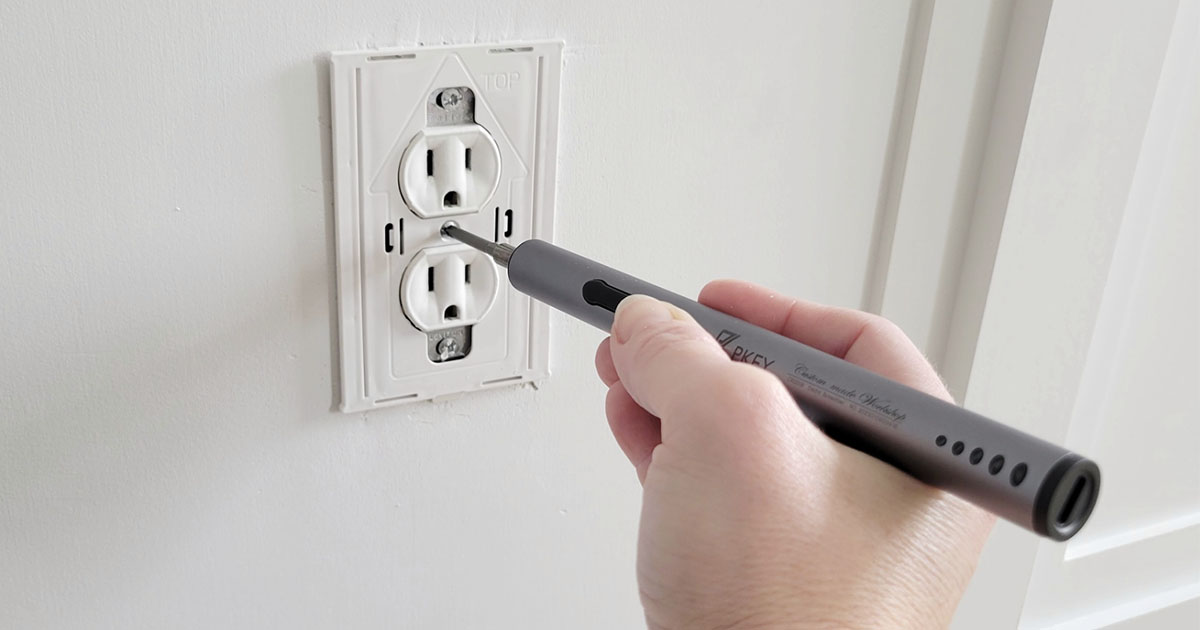 hand holding PKEY scredriver screwing screw into wall outlet