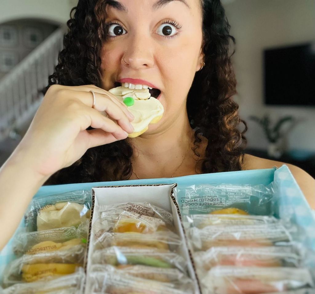 woman holding box of cheryl's cookies biting into sugar cookie