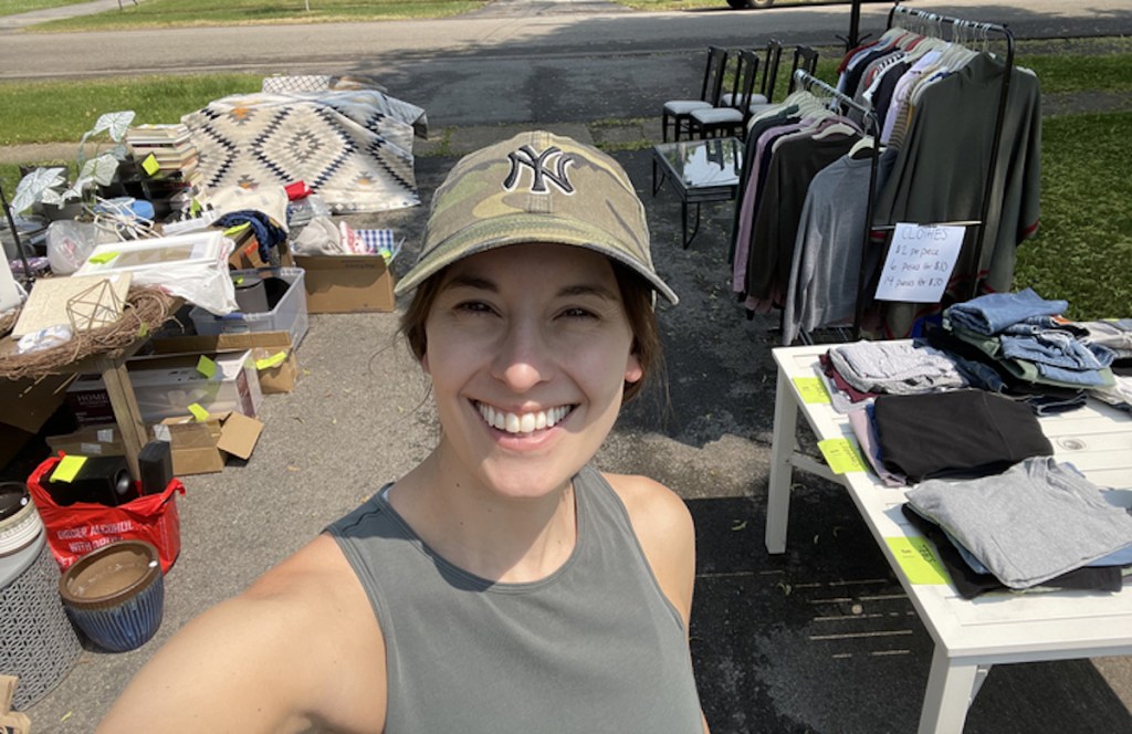 woman taking selfie in front of driveway yard sale