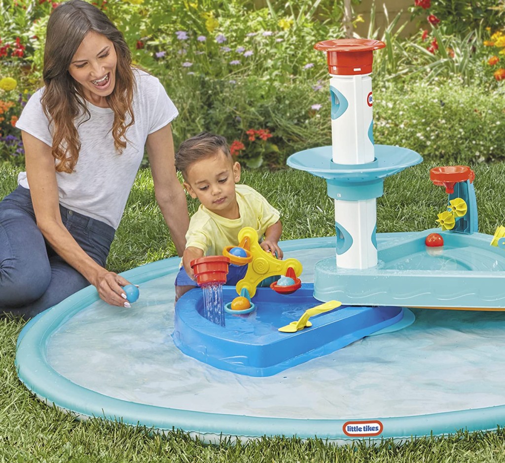 mom sitting next to little boy in splash pad