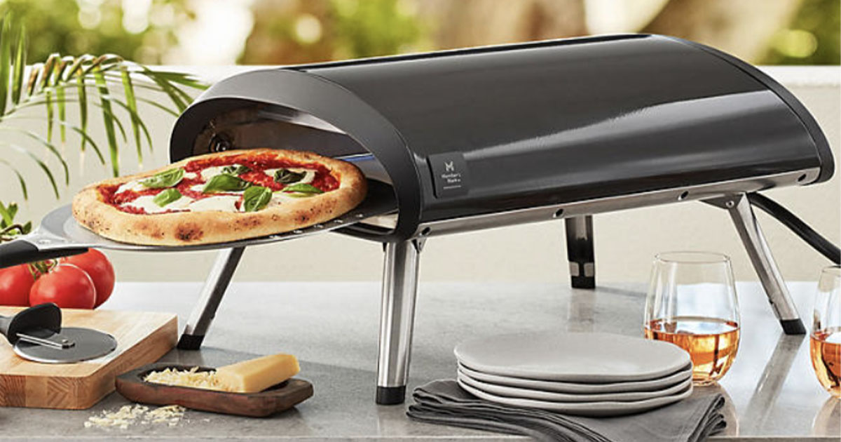 black pizza oven with pizza onlineing out of it on table with plates