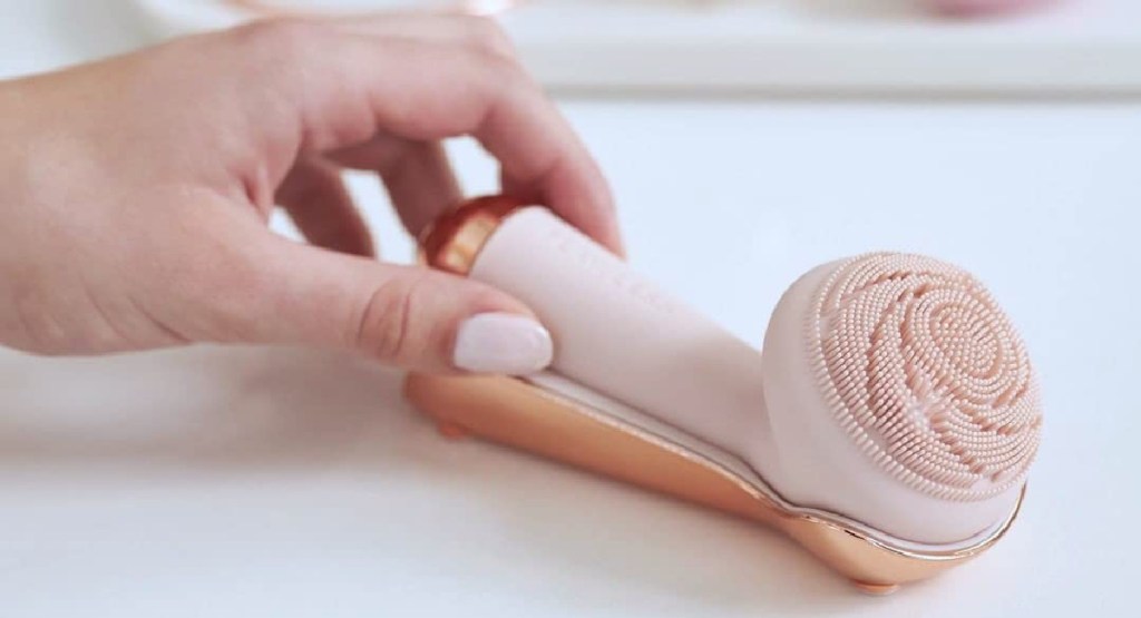 silicone cleansing tool on charger with hand holding it