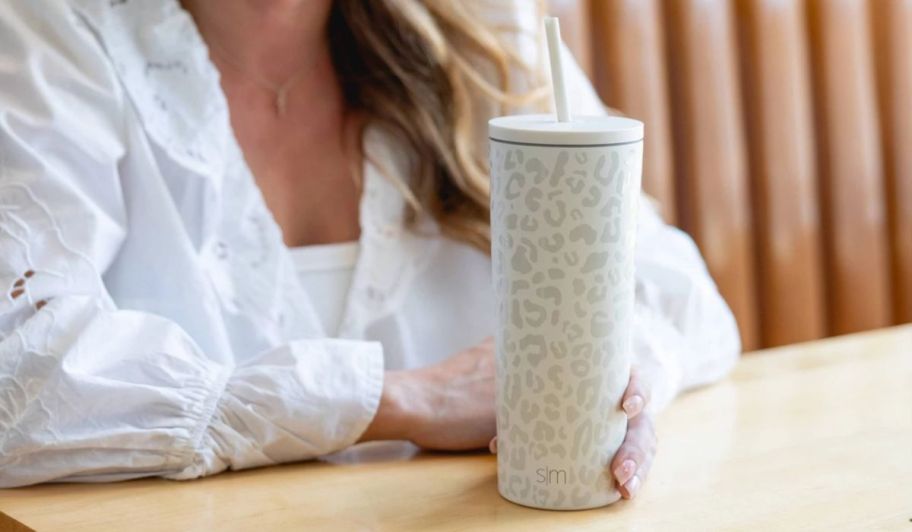 a woman seated at a table with a cream leopard colored simple modern insulated tumbler